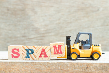 Toy forklift hold letter block m to complete word spam on wood background