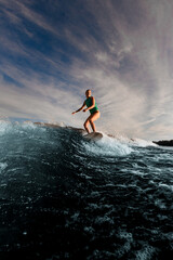 happy female wakesurfer vigorously riding on wakeboard down the river waves against the blue sky.