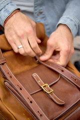 Cropped Male hands opening leather brown backpack, style and fashion concept. outdoors close-up photo. leather accessory, handmade backpack
