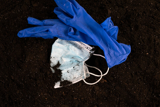 a used, old medical face mask and blue gloves in the ground. Ecological problems. Environmental pollution