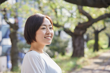 早朝の新緑の中でほほ笑む40代日本人女性