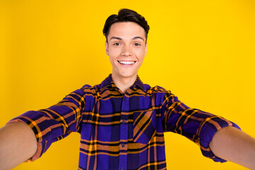 Photo of charming funny teenager man dressed checkered clothes recording self video smiling isolated yellow color background