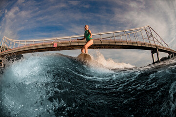 great view of woman wakesurfer riding down on the board on splashing wave against bridge.