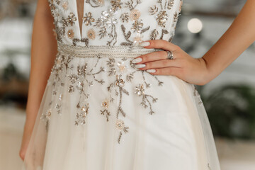 Hands of a woman in a white dress, decorated with beads, sequin embroidery and stones