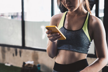 close up young fit woman using smart phone at gym