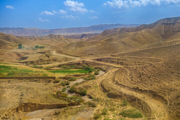 Fototapeta na wymiar Semi-dry river, winding between hills in the middle of an almost deserted area. The mountains of the Gissar ridge are visible in the distance. Shot in the Surkhandarya region of southern Uzbekistan