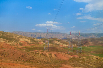 Power transmission towers in middle of colorful hills. Mountain range is visible in distance. Shot in Surkhandarya region in Uzbekistan near mountains of Gissar ridge
