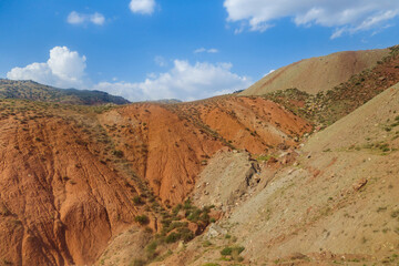 Red hills in foothill valley against bright blue cloudy sky. Shot in Surkhandarya region in Uzbekistan near mountains of Gissar ridge