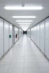 Obraz premium Long empty illuminated interior hallway. Vanishing perspective, bright neon lights, vertical cabinets lined side wall. Underground, no people