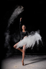 Obraz na płótnie Canvas Dramatic portrait of strong and talented female dancer with white powder explosion, moving in dust, flour. Graceful gorgeous woman in black bodysuit in slow motion