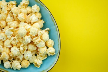 Popcorn with spices in a blue plate on a yellow background top view. Salted popcorn with cheese flavor  in a bowl, place for text. Corn grains from Argentina that are popping open.