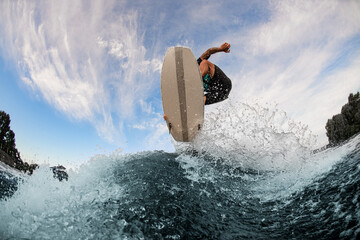 beautiful view of a wakesurf board and man jumping in the air above a splashing wave