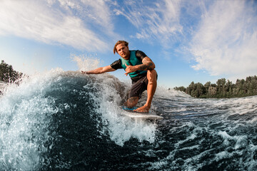 athletic guy wakesurfer skilfully riding down the blue splashing wave on a warm day
