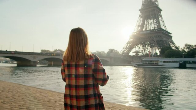 Backside view of Woman taking Picture by Smartphone of Eiffel Tower in Paris, France on Sunny Day. Travel and Tourism in Europe, Sightseeing of European Landmarks. 4K Medium gimbal shot