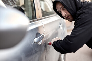 side view of caucasian auto thief guy, looking around, afraid to be caught, at street. Young male...