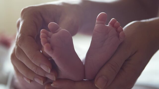 Close-up feet of a nursing baby who has recently been born. Newborn infant boy at home. Window light.