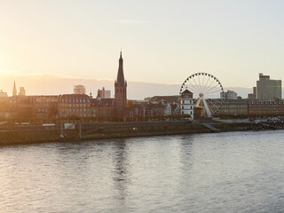 Fototapeta premium Panorama view of the city of Dusseldorf from the Rhine in Germany. Skyline of the old town with Ferris wheel at sunrise.