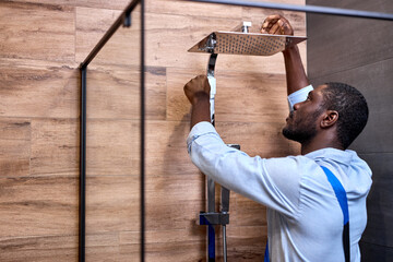 Afro american Professional handyman working in shower bath indoors, side view portrait, handsome...