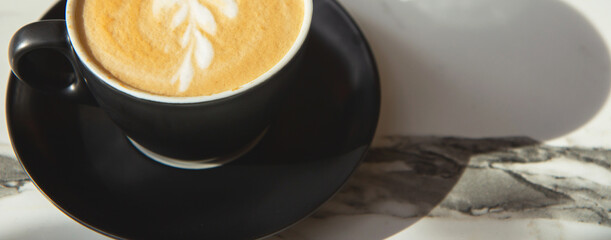 Black ceramic cup of coffee on a marble table on an open terrace in bright sunlight