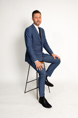 Full length portrait of man in suit sitting on chair, isolated on white background