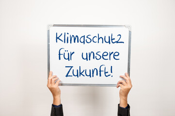 Hände halten eine Tafel hoch auf der Klimaschutz für unsere Zukunft steht