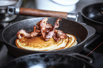 Pancakes with crispy bacon in cast iron skillet, frying pan. Morning Breakfast.