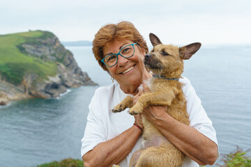 Cheerful elderly woman holding a brown dog. Horizontal view of elderly woman with her pet dog on holidays outdoors. Retirement people and dog concept.