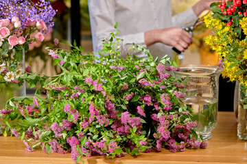 Bouquet of wild spring flowers lying on table made for bouquet, close-up photo. female florist in the background at work place, arranging fresh flowers for sale. copy space.