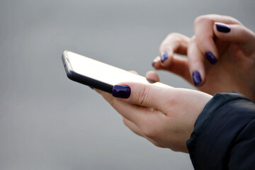 Female hands with smartphone close up on blurred background. Woman with manicure using mobile phone on a street in cold weather