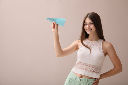 Beautiful teenage girl with paper plane on beige background. Space for text