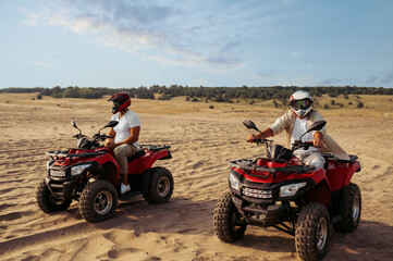 Fototapeta na wymiar Two men in helmets ride on atv in desert