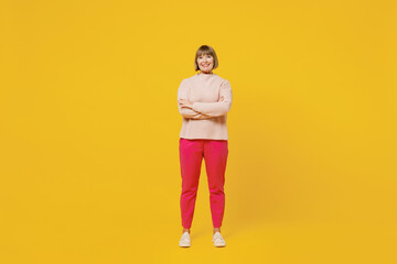 Fototapeta na wymiar Full body elderly smiling happy woman 50s with bob haircut wears pink casual knitted sweater hold hands crossed folded isolated on plain yellow background studio portrait. People lifestyle concept