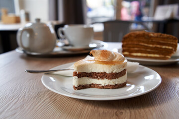 Cake with mascarpone on a table in a cafe, with a teapot in the background