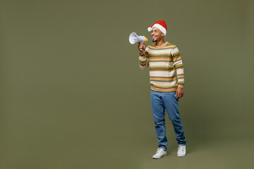 Full body young african man in sweater red Christmas hat hold scream in megaphone announces...