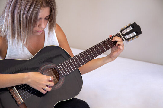 Chica tocando la guitarra en su habitación. Mujer mirando su guitarra española mientras toca en su casa. Mujer practicando un hobbie. Estilo de vida