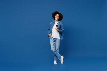 Full body young fun smiling happy black woman in casual clothes shirt white t-shirt hold takeaway delivery craft paper brown cup coffee to go isolated on plain dark blue background studio portrait