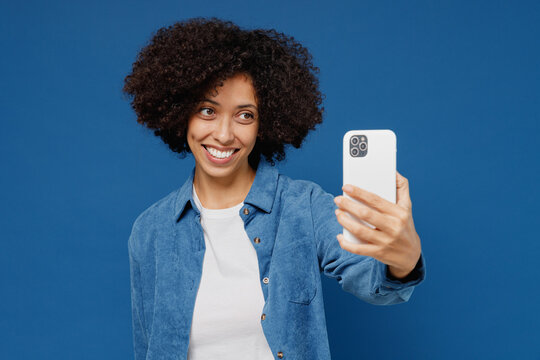 Young fun happy black woman in casual clothes shirt white t-shirt doing selfie shot on mobile cell phone post photo on social network isolated on plain dark blue background. People lifestyle concept.