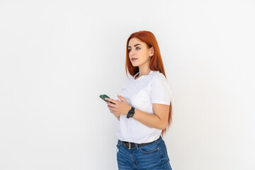 Pleased smiling red haired woman holds cell phone over white background