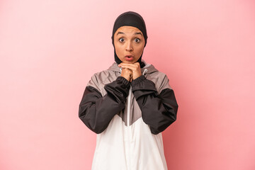 Young Arab woman with sport burqa isolated on pink background praying for luck, amazed and opening...