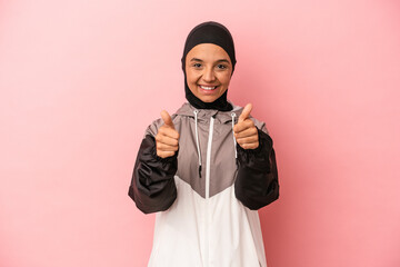 Young Arab woman with sport burqa isolated on pink background with thumbs ups, cheers about...