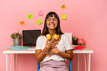 Young mixed race woman preparing a exam in the room listening to music isolated on pink background laughs happily and has fun keeping hands on stomach.