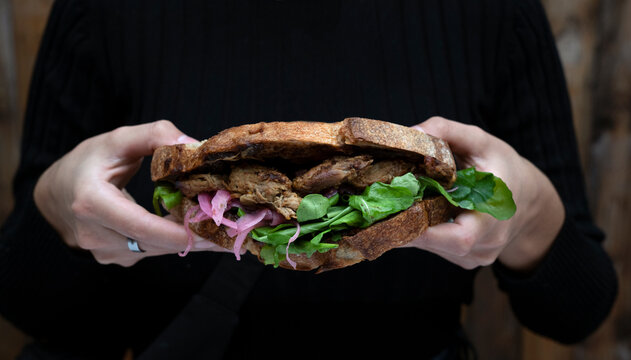 Young woman holding a pork meat braised bondiola sandwich with lettuce and red onion pickles.