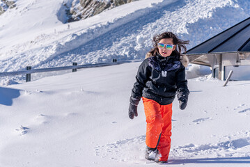 Fototapeta na wymiar Child walking in snow. One Asian girl in ski-wear, sunglasses and gloves playing in winter.