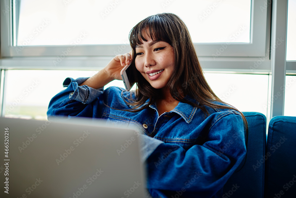Poster funny asian woman with netbook technology enjoying mobile conversation with friend, happy freelancer
