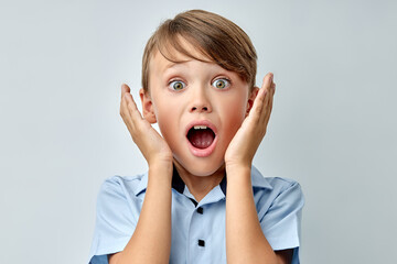 caucasian little boy amazed touching face with opened mouth isolated gray color background. Adorable young boy in shock, looking at camera in disbelief. Shock, amazement, surprise concept.
