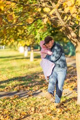 Dad holds his one-year-old daughter in his arms and kicks the leaves in the autumn grove.