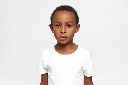 Serious African American kid, having focused and concentrated face, looking at camera with sadness, worry and melancholy in his big deep brown eyes. Kids and their attitude, feelings, emotions