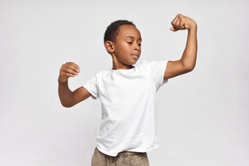 Portrait of strong confident dark-skinned boy, contracting upper arm muscles, showing biceps and...