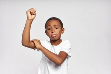 Horizontal picture of sad dark-skinned boy showing his weak muscles, feeling disappointed, upset...