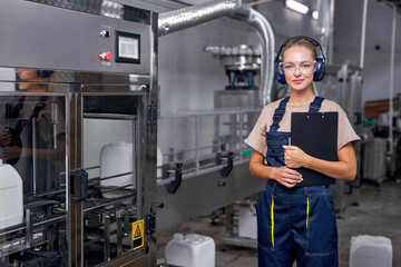 Confident industrial woman engineer in spectacles standing in factory at work place, dressed in blue uniform, holding paper in hands. pesticides production in factory. female engineer look at camera